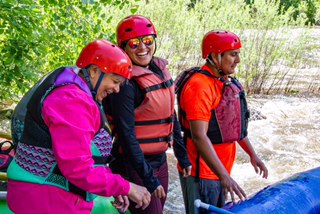 A trio of individuals in helmets and orange vests stands in a raft, poised for an exciting experience on the water.